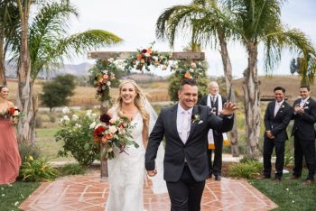 Wedding couple walking down the aisle with joyful expressions while guests look on.