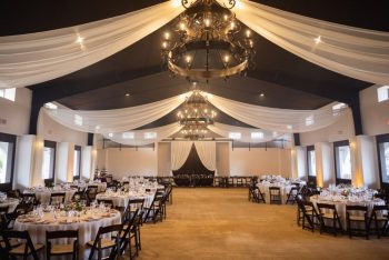 Elegantly set dining hall with chandeliers and draped ceiling fabric before an event.