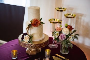 Elegant wedding cake decorated with flowers, displayed on a table with coordinating floral arrangements and candle holders.