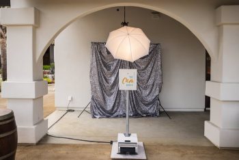 A photo booth setup with a glittery backdrop and an umbrella light in an outdoor archway.