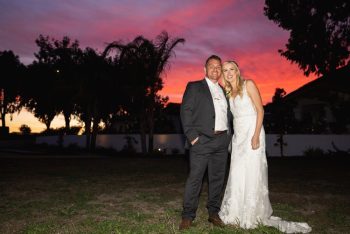 Couple smiling at sunset with colorful sky in the background.
