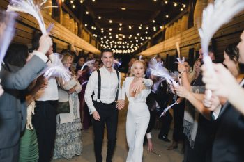 A newlywed couple walking through a cheerful crowd holding sparklers.
