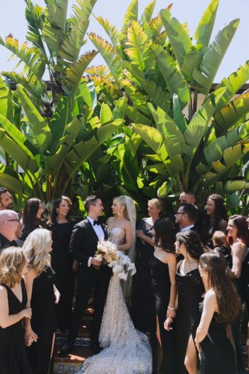 Wedding couple exchanging vows surrounded by guests and lush greenery.