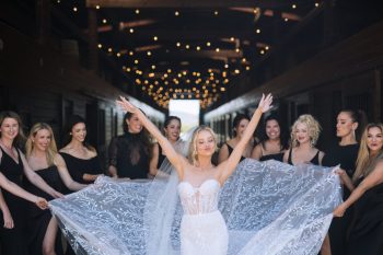 Bride and bridesmaids celebrating in a wooden corridor with string lights.
