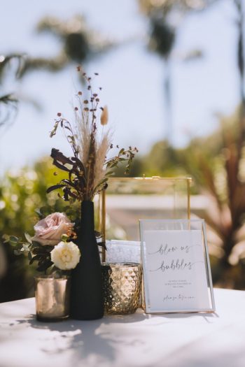 Elegant event table setting with floral arrangement and a "blooms & bubbles" sign.
