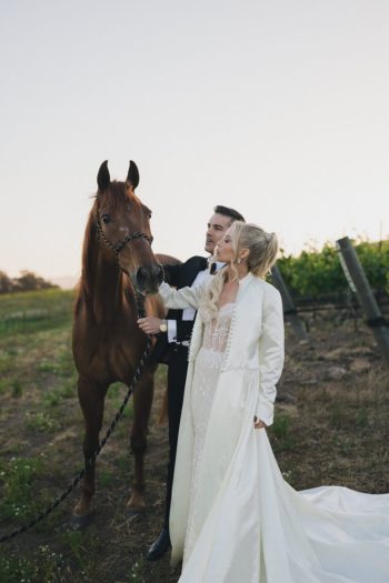 Bride and groom posing with a horse in a pastoral setting.