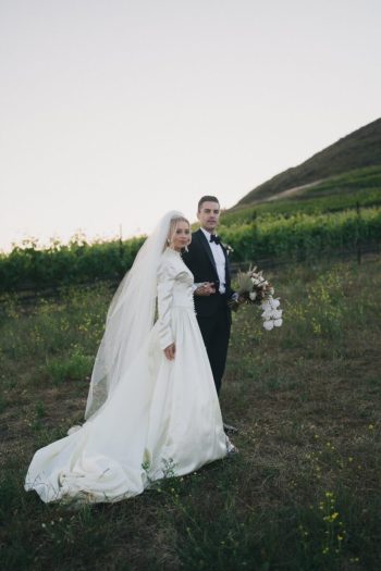 A bride and groom posing for a photograph in a vineyard.