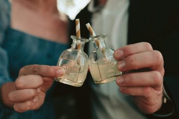 Two individuals holding miniature patron tequila bottles with straws.