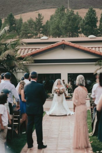 Bride walking down the aisle at an outdoor wedding ceremony.