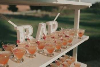An outdoor bar setup with a selection of cocktails garnished with flowers.