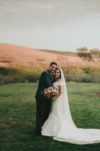 Bride and groom smiling outdoors with a bouquet.