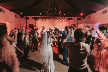 A bride and groom dancing to live music surrounded by cheering guests at a wedding reception.